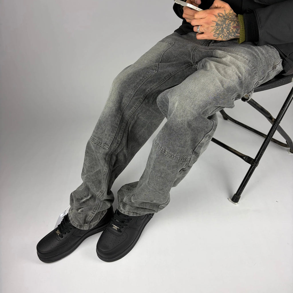 Modelo sentado usando jeans carpintero gris Stylo 88 con zapatillas negras, look streetwear