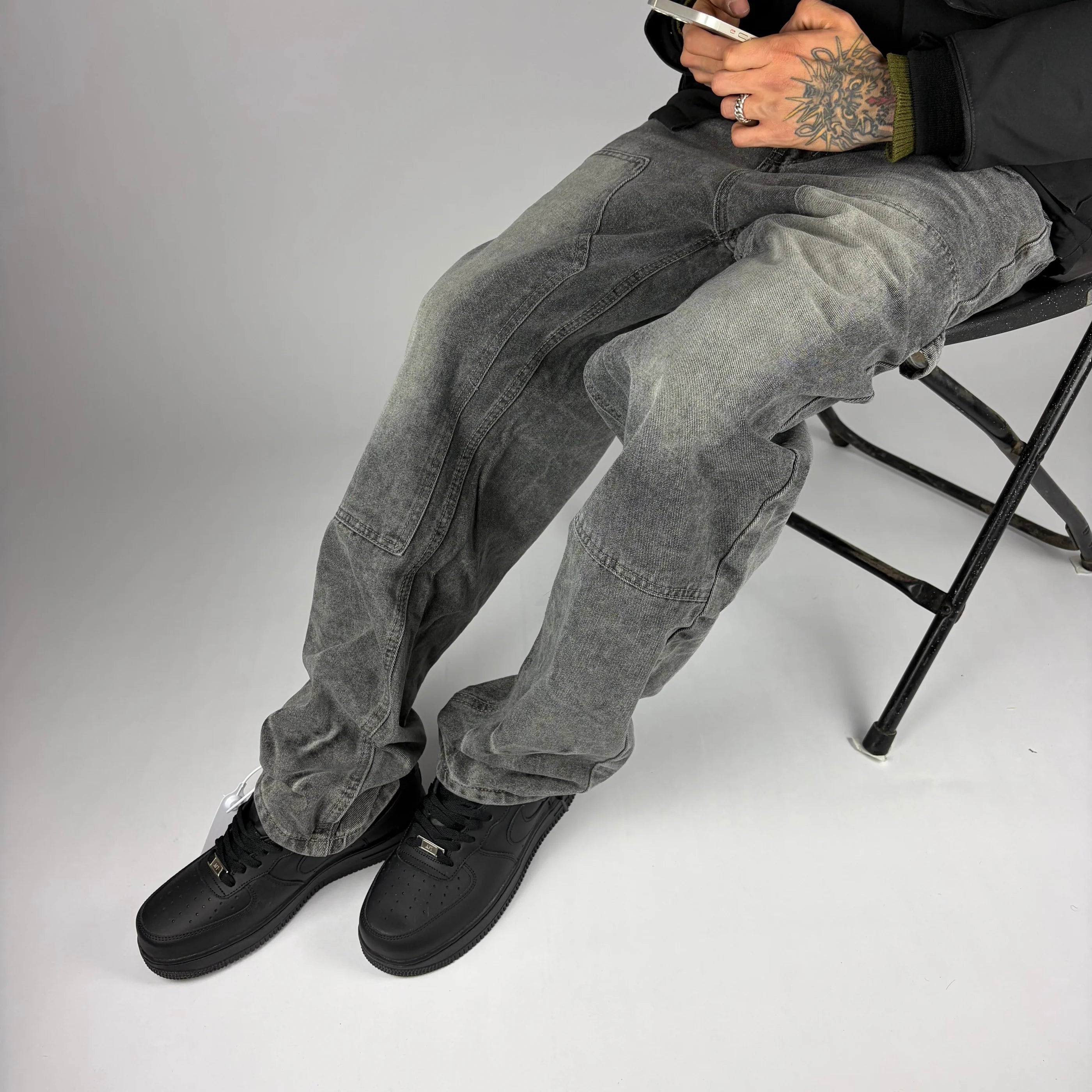 Modelo sentado usando jeans carpintero gris Stylo 88 con zapatillas negras, look streetwear